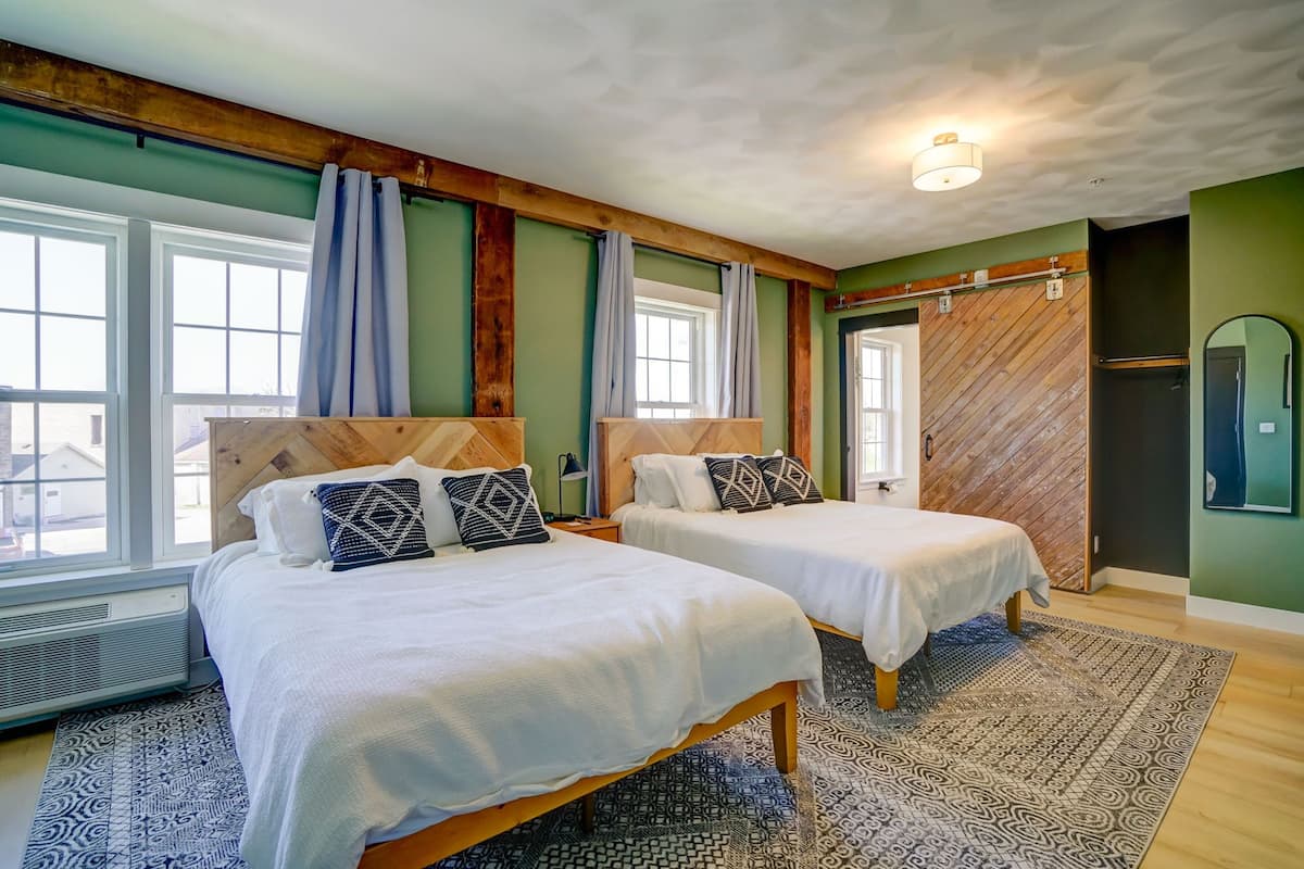 A room with two beds, a large window, and a wooden ceiling.