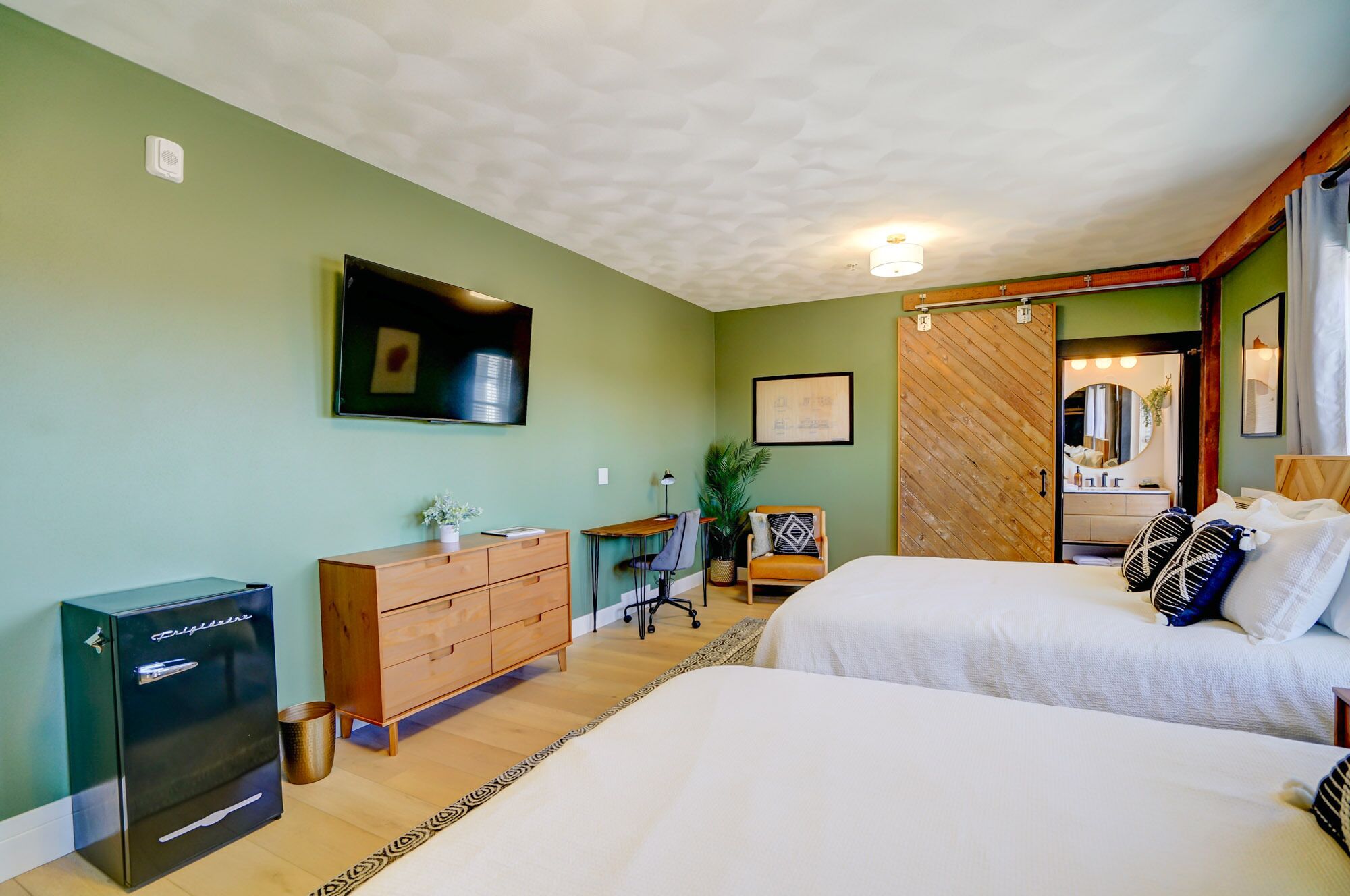 Une chambre avec deux lits, un bureau, une commode, un réfrigérateur et un luminaire au plafond.