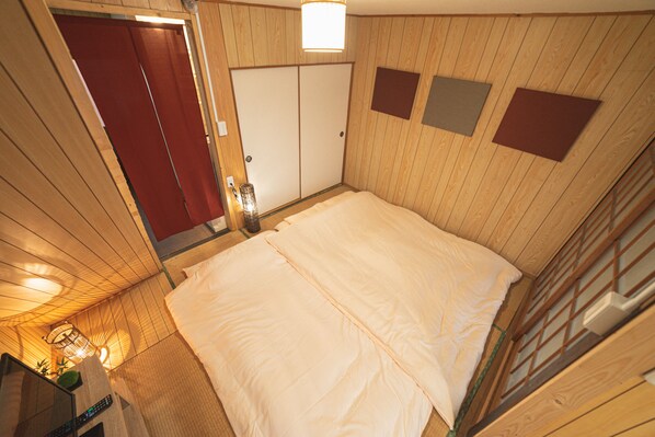 A bedroom with a large bed, wooden walls, a red door, and a small table with a plant.