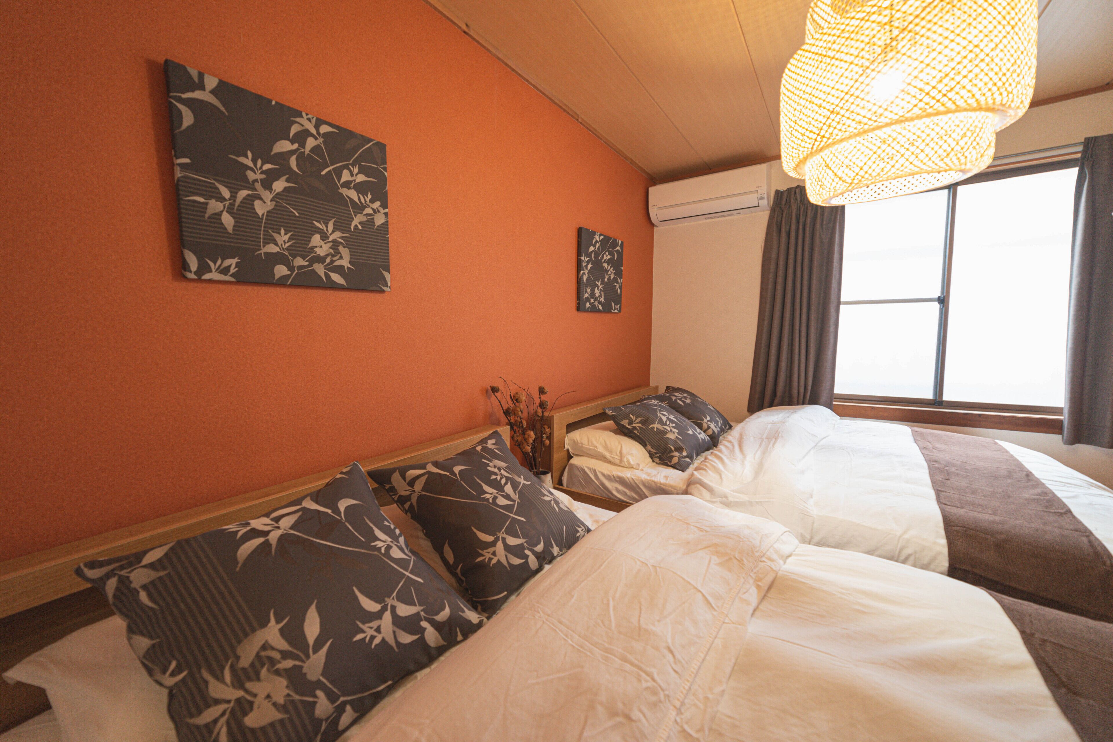 Een hotelkamer met twee bedden, een groot raam met gordijnen en kunstwerken aan de muur.