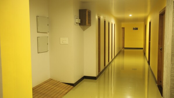A long, narrow hallway with yellow walls and a wooden floor. There are multiple doors on one side and a wall-mounted air conditioning unit on the other. - Hotel Vijayetha (Nagercoil)