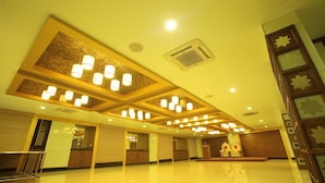 A spacious lobby with a high ceiling, multiple chandeliers, and a stage with ornate chairs. - Hotel Vijayetha (Nagercoil)