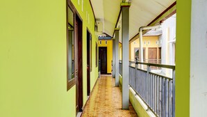 Un couloir au sol carrelé, aux murs verts et doté d’un balcon avec une rambarde en métal.