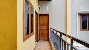 Un couloir étroit, avec une porte en bois au bout, un sol carrelé et une rambarde en métal d’un côté.