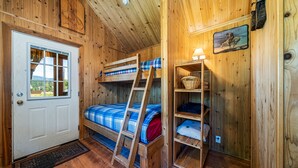 Una cabaña de madera con literas, una escalera, una puerta con ventana y un estante con lámpara.
