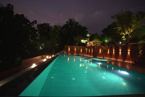 Una piscina con superficie de baldosas, rodeada por una valla de madera e iluminada con luz ambiental.