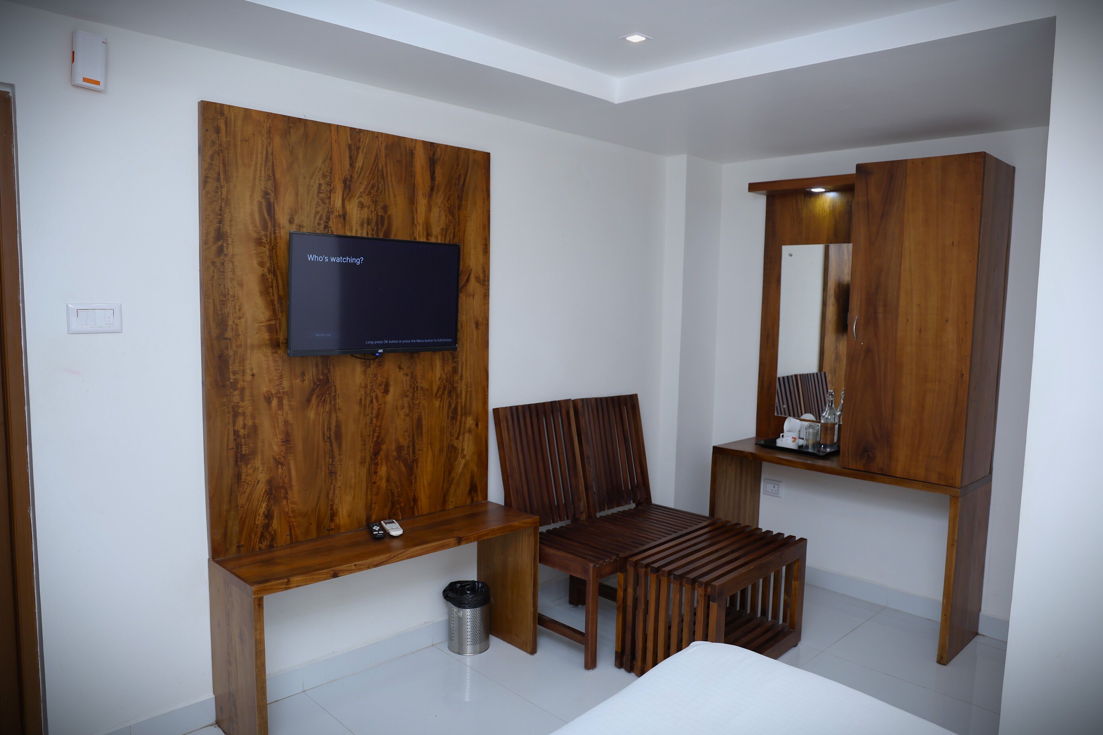 Una habitación moderna con un mueble de pared de madera, un televisor, una silla, una mesita y un espejo.