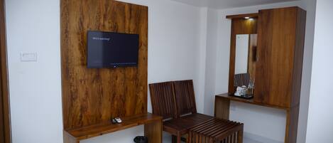 Una habitación moderna con un mueble de pared de madera, un televisor, una silla, una mesita y un espejo.