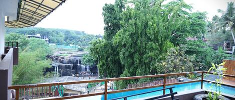 A balcony with a view of a waterfall, lush greenery, and a pool.