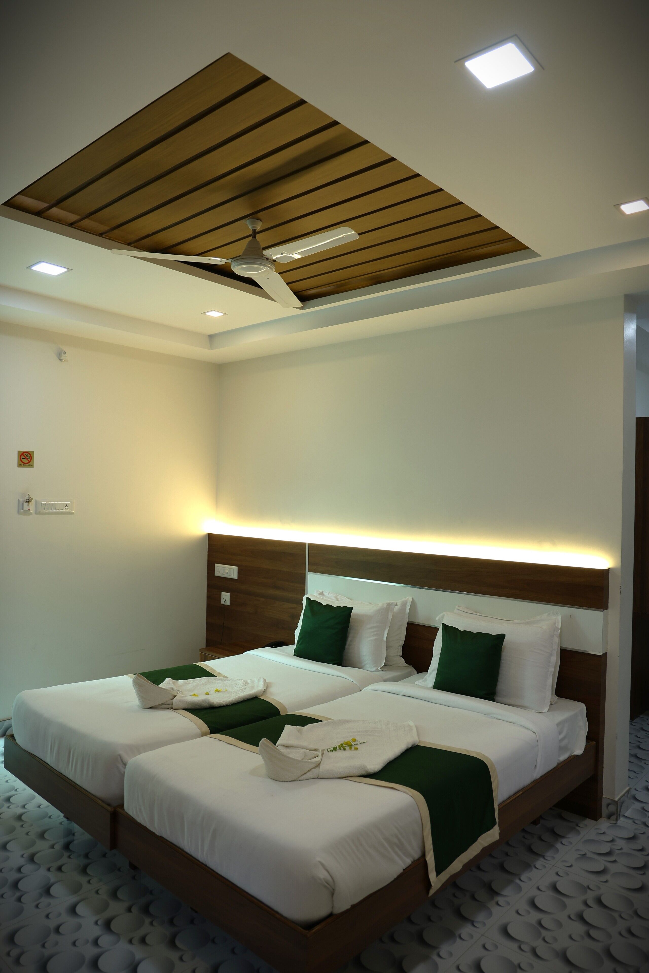 Habitación de hotel con cama, ventilador de techo, iluminación empotrada y techo de madera.