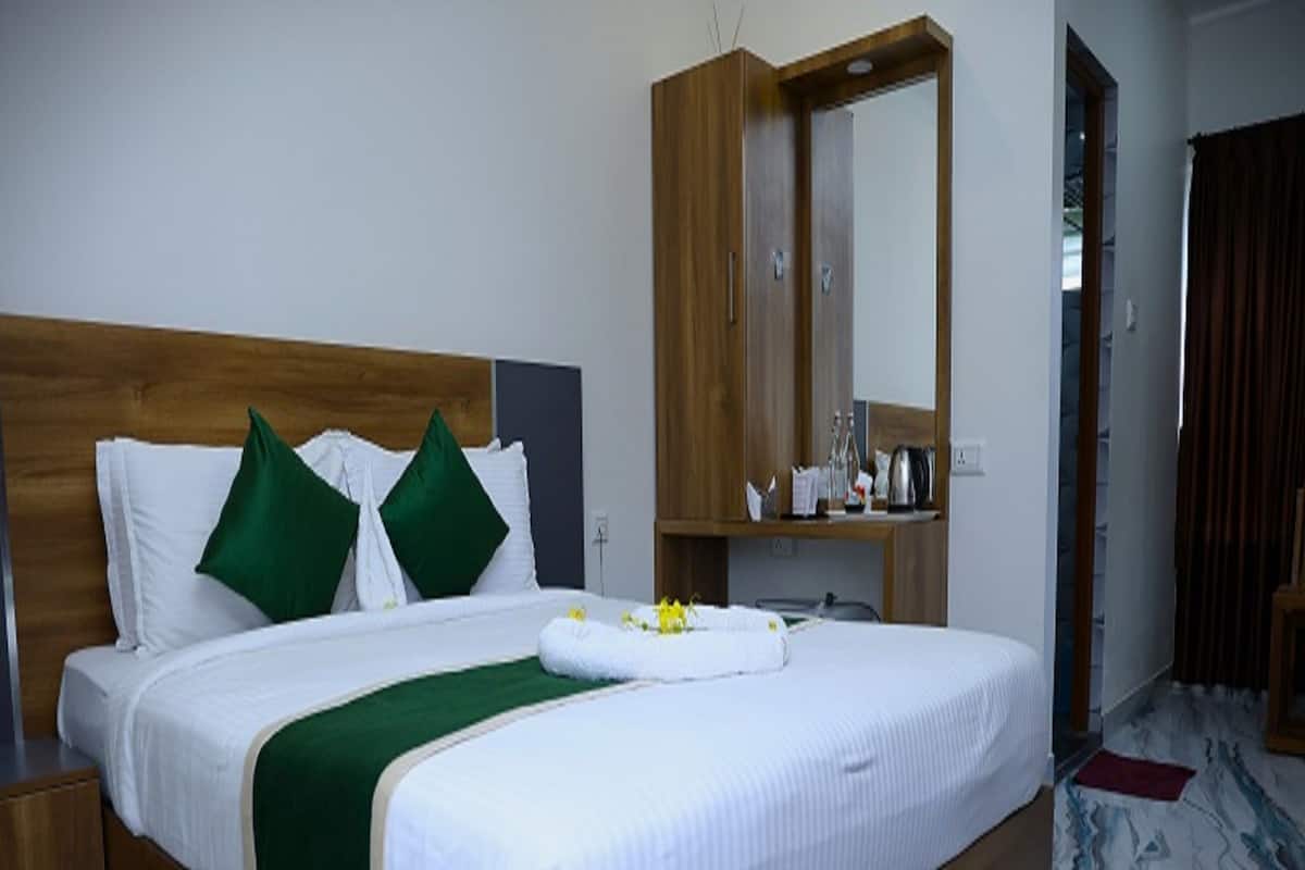 Habitación de hotel con cama de madera, almohadas verdes, cubrecama blanco, mesita de noche de madera, espejo y suelo de mármol.
