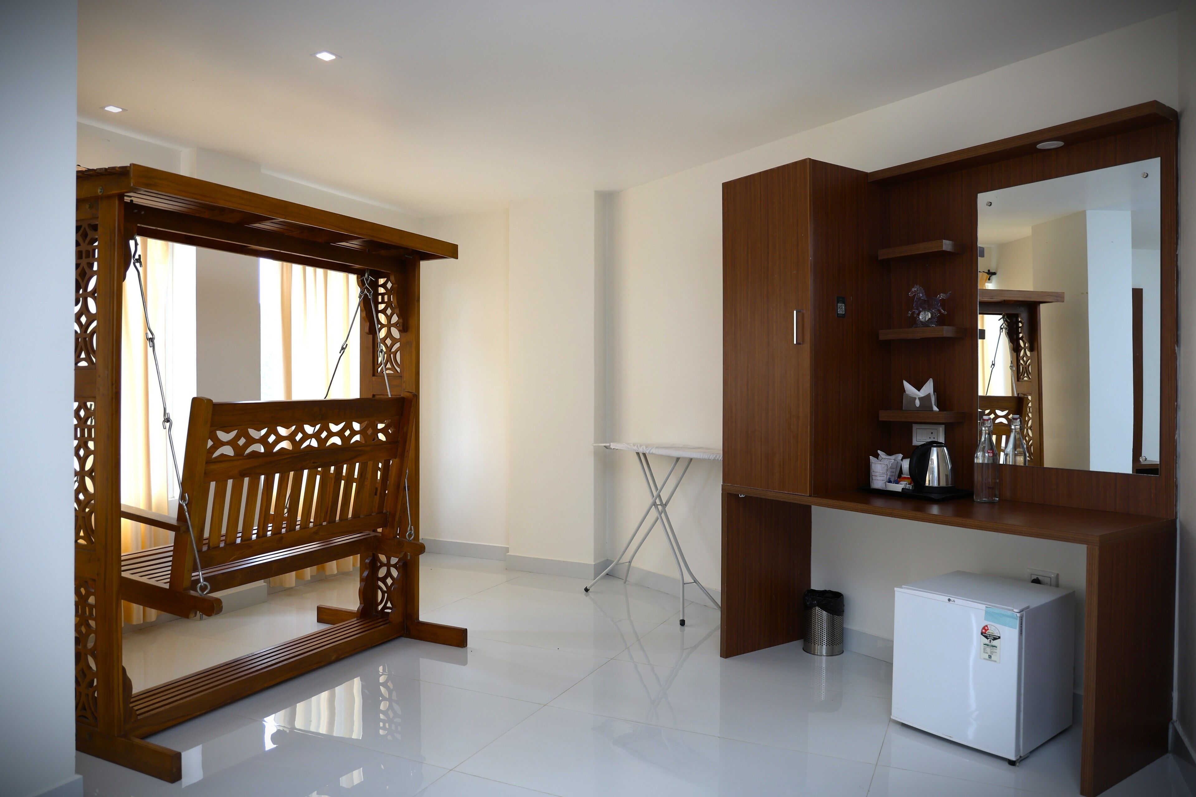 A room with a wooden bench, a small white refrigerator, and a wooden cabinet with shelves.