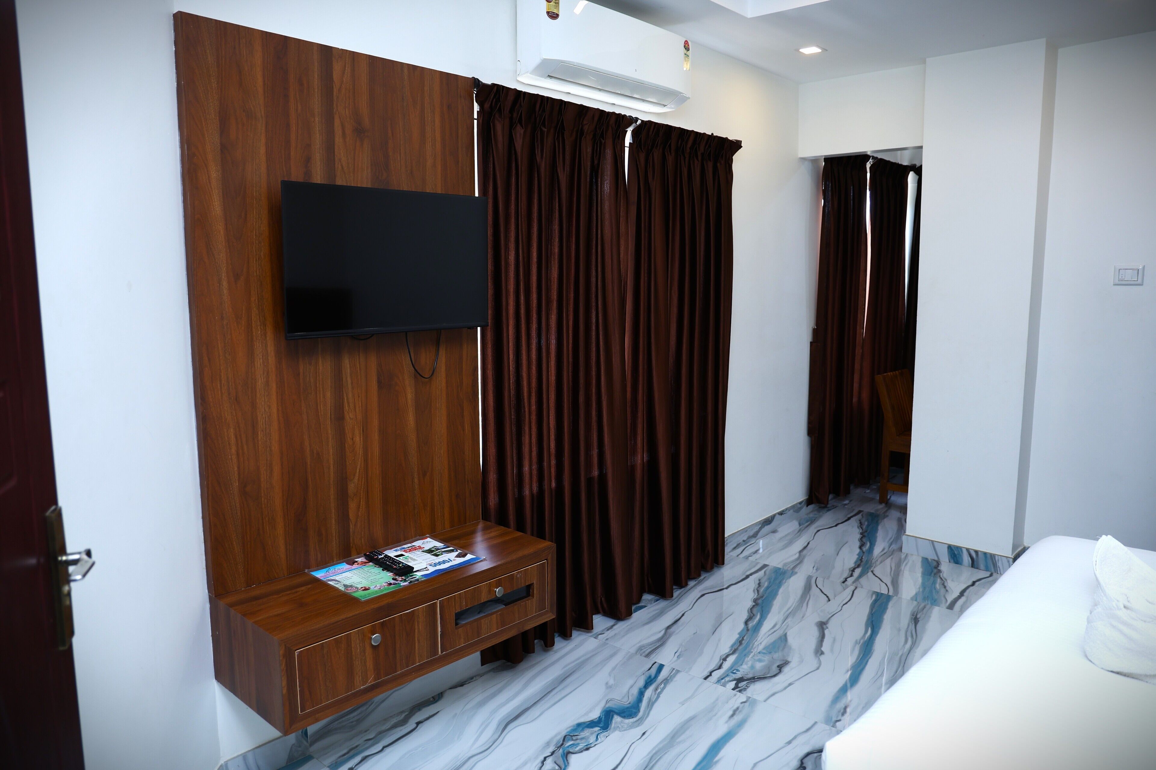 A hotel room with a wooden cabinet, a flat-screen TV, a marble-patterned floor, and a bed.