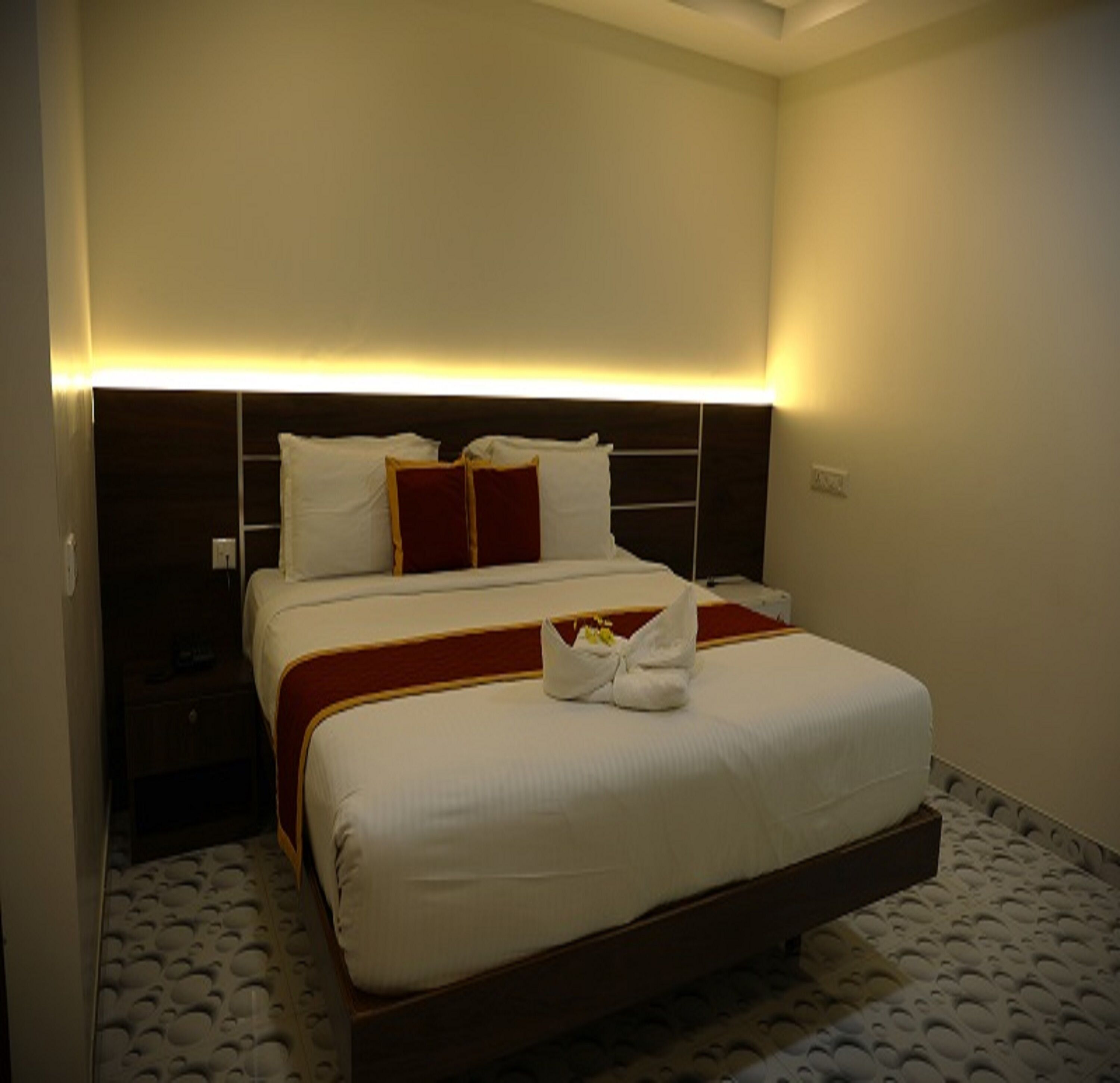 A hotel room with a large bed, a nightstand, and a wall-mounted light fixture.