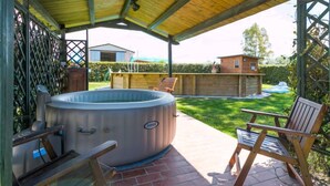 Un espacio de patio al aire libre con un jacuzzi, dos sillas de madera y una estructura de techo cubierta.