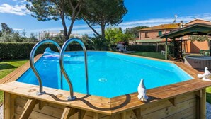 Una piscina rectangular con muelle de madera y escaleras metálicas, rodeada de césped y árboles.