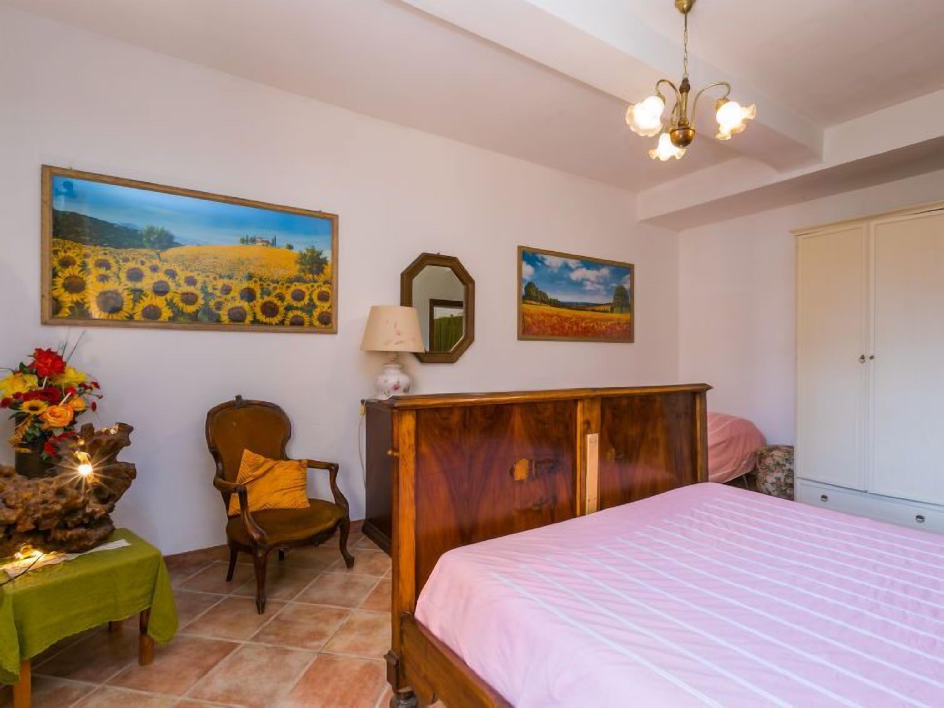 Een slaapkamer met een bed, een stoel, een dressoir en twee schilderijen aan de muur.