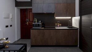 Cocina compacta con microondas, lavamanos y horno empotrado. Incluye una pequeña encimera y un mueble de madera oscura.