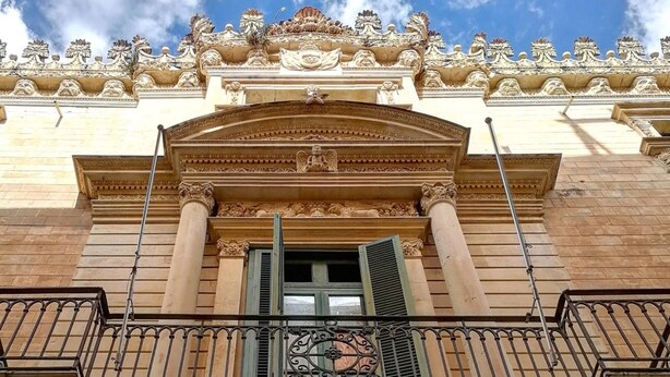 Fachada de edificio con detalles arquitectónicos ornamentales, un balcón con barandilla de hierro forjado y una ventana con contraventanas.