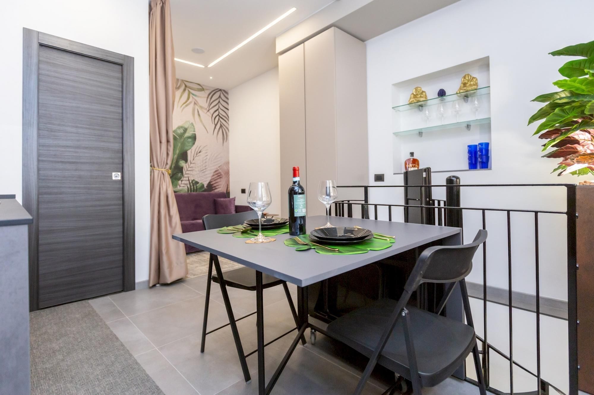 A modern dining area with a table set for two, a bottle of wine, and a glass.