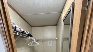 Un pasillo estrecho con suelo de madera, una puerta metálica y una pared blanca con un perchero.