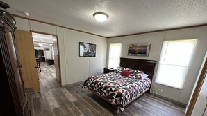 Un dormitorio con una cama grande, suelo de madera, una puerta que da a otra habitación y una lámpara en el techo.
