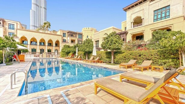 A swimming pool with lounge chairs, a children's play area, and a view of a tall skyscraper. - Charming 2 Bed l Old Town Dubai l Memorable stay (Downtown Dubai)