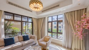 A spacious living room with a sofa, armchair, and coffee table, large windows with curtains, and a decorative chandelier. - Charming 2 Bed l Old Town Dubai l Memorable stay (Downtown Dubai)