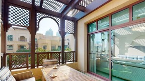A balcony with a wooden table and chairs, a cushioned sofa, and a view of buildings in the background. - Charming 2 Bed l Old Town Dubai l Memorable stay (Downtown Dubai)
