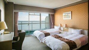 Ein Hotelzimmer mit zwei Betten, einem Schreibtisch, einem Stuhl und einem großen Fenster mit Meerblick.
