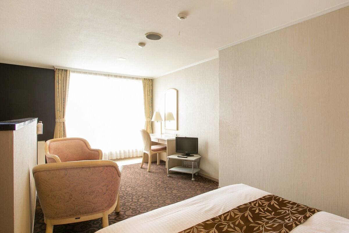 A hotel room with a bed, a desk with a computer, a chair, and a television.