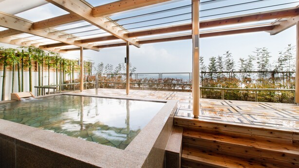 Ein moderner, überdachter Pool mit Holzbalken und Glasfenstern, umgeben von einer Holzterrasse und Bambuspflanzen.