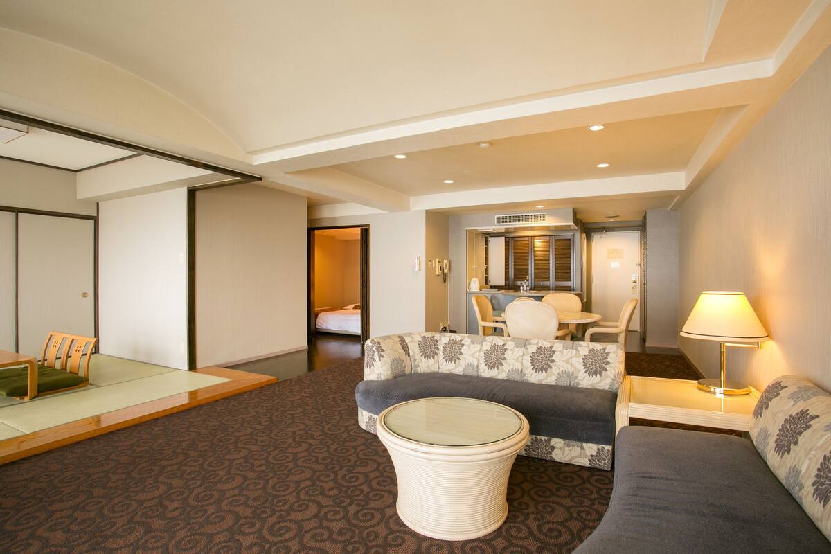 A hotel room with a sofa, a small table, a chair, a bed, and a bathroom visible through an open door.