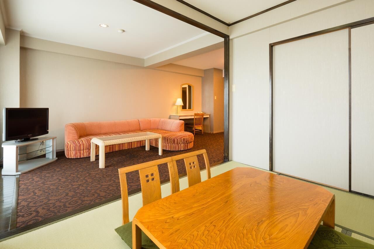 Una habitación de hotel moderna con una mesa de comedor de madera, un sofá, un televisor y una puerta corredera.