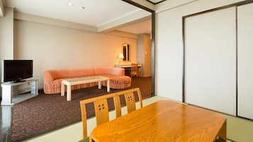 Una habitación de hotel moderna con una mesa de comedor de madera, un sofá, un televisor y una puerta corredera.