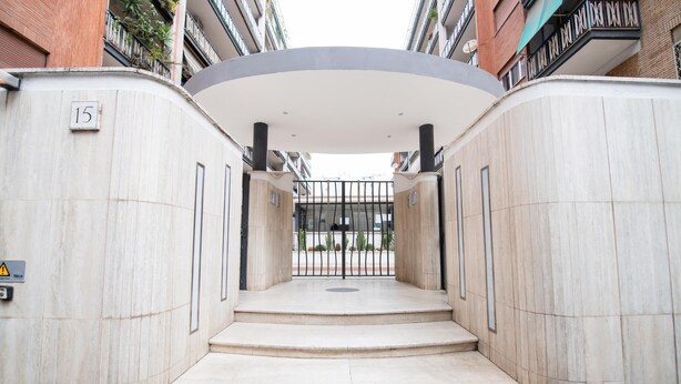 Entrada de um edifício moderno com telhado curvo, portão e placa com o número 15.