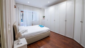Um quarto com cama, mesa de cabeceira com abajur, guarda-roupa e janela com cortinas.