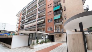 Um edifício residencial com vários andares, varandas, entrada coberta e um pátio ladrilhado.