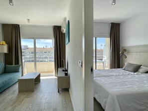A hotel room with a bed, a sofa, a small table, a TV, and a balcony with a view of buildings. - FESTASTAR 406 (Estartit)