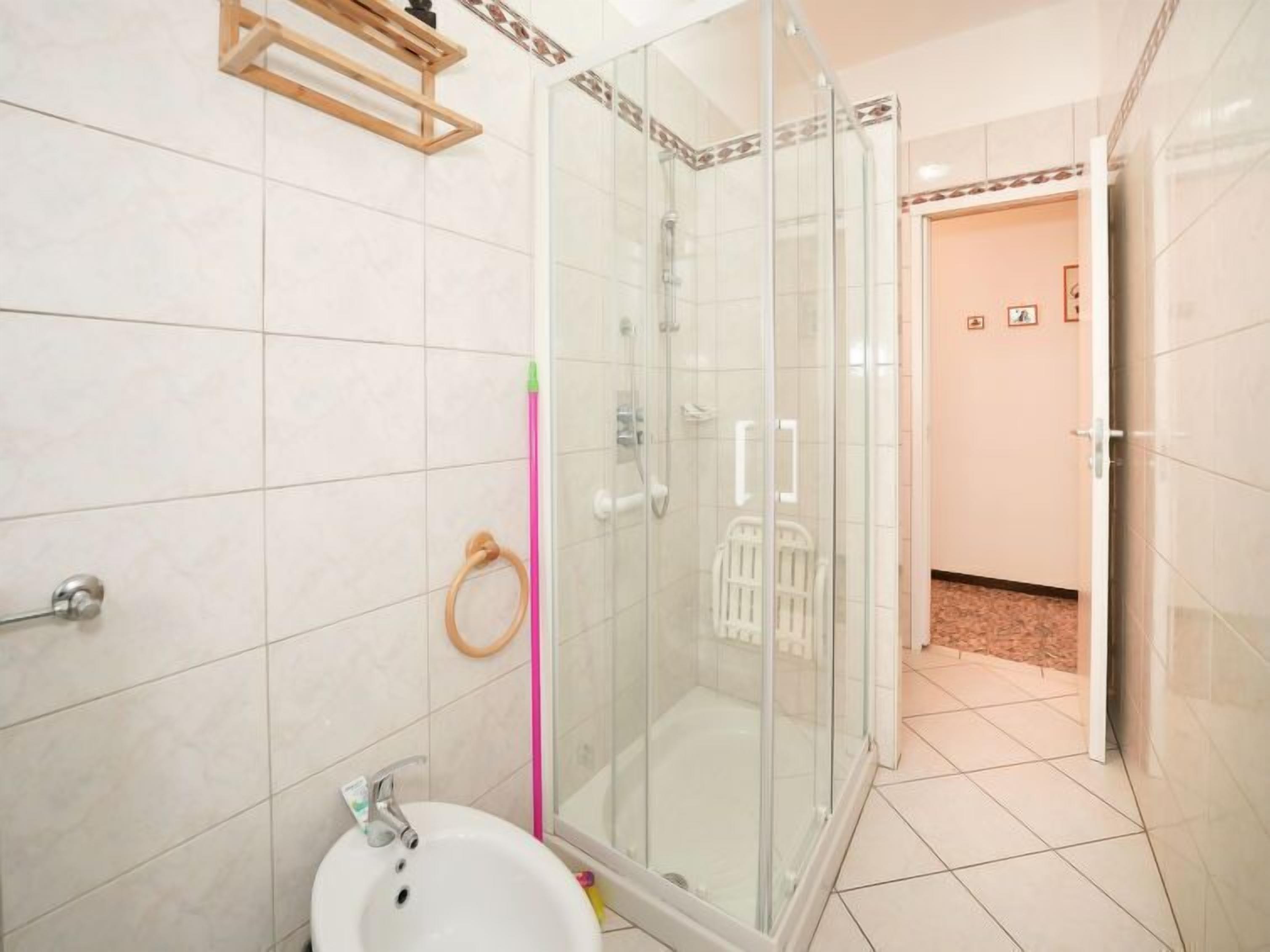 Ein modernes Badezimmer mit einer Duschkabine aus Glas, einem weißen Waschbecken und einem hölzernen Handtuchhalter.