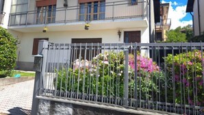 Ein zweistöckiges Gebäude mit Balkon, geschlossenem Eingangsbereich und einem Garten mit rosa Blumen.