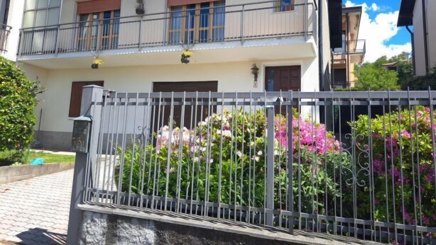 Een gebouw met twee verdiepingen, een balkon, een hekpoort en een tuin met roze bloemen.
