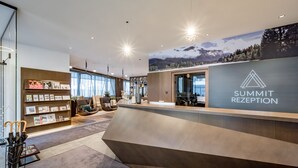 A modern reception area with a wooden reception desk, a wall-mounted display of brochures, and a large window providing natural light.