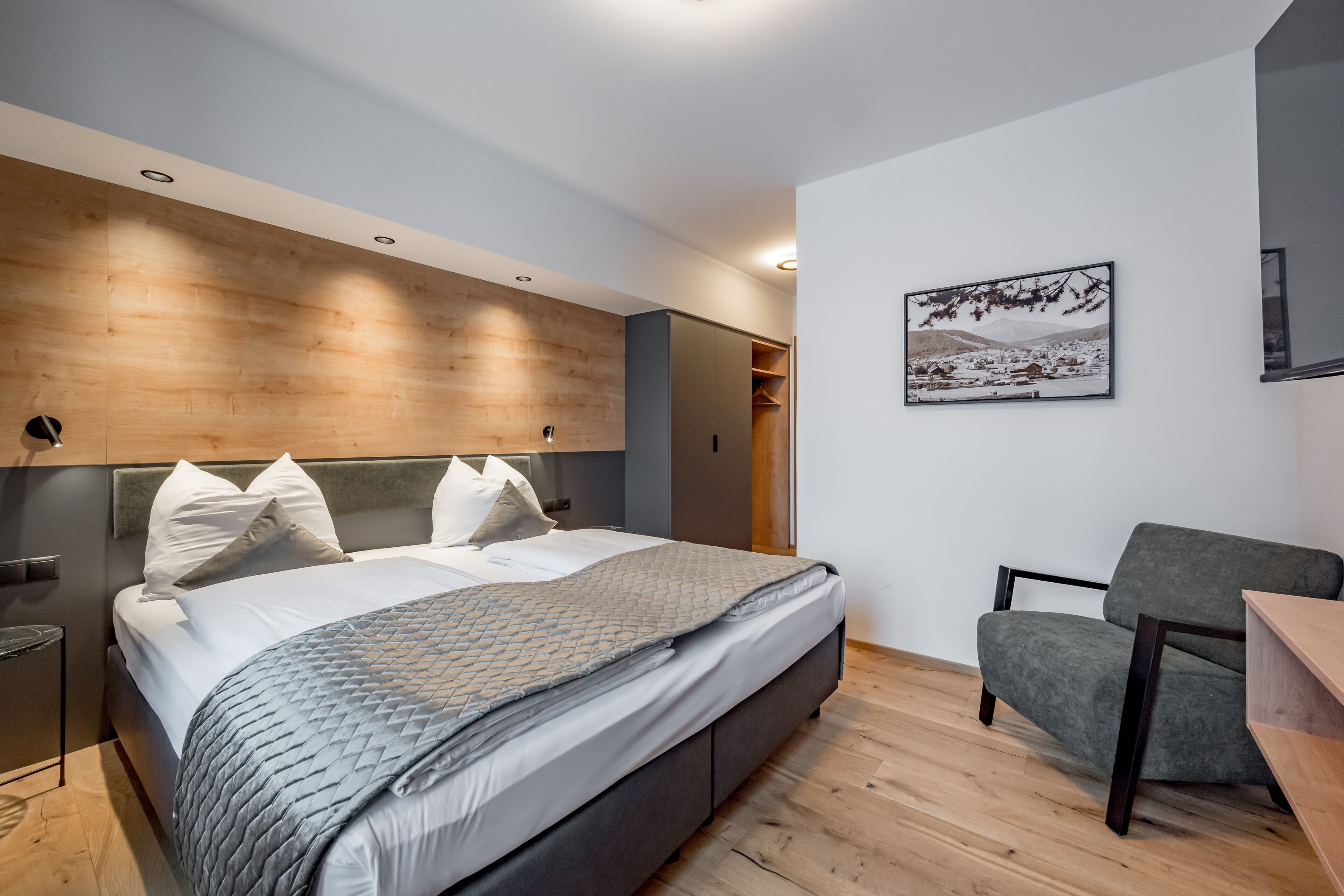 A modern bedroom with a large bed, a grey armchair, and a wooden headboard.
