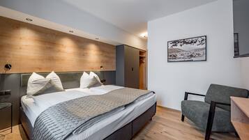 A modern bedroom with a large bed, a grey armchair, and a wooden headboard.