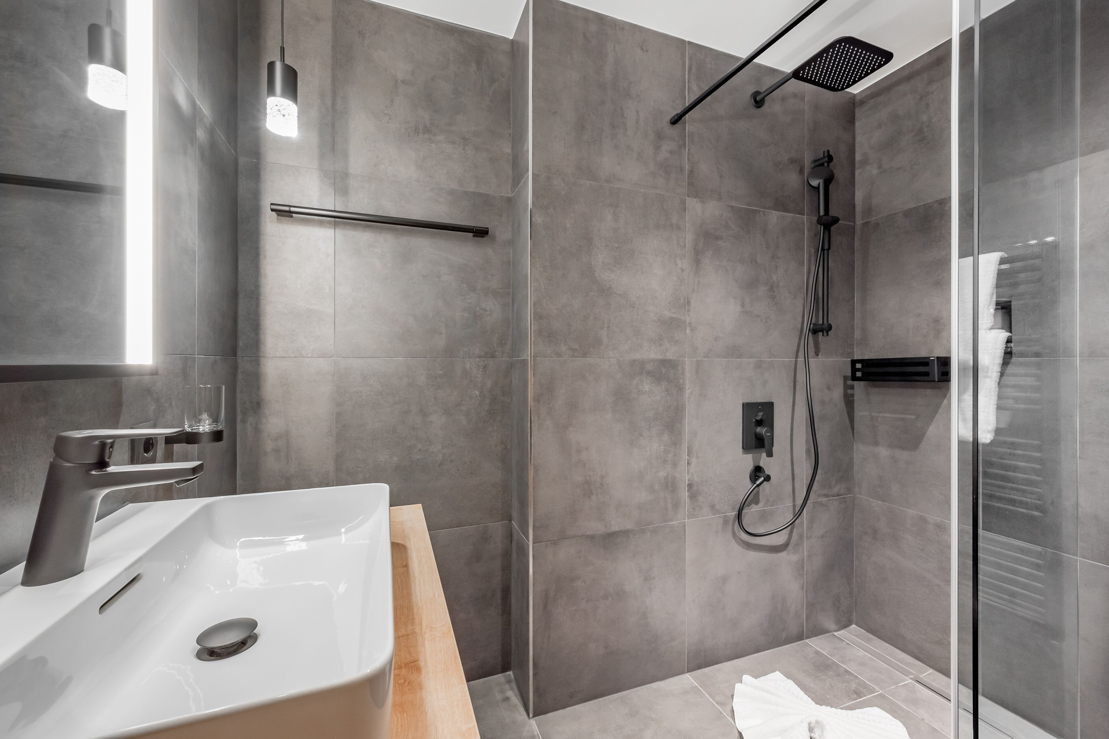A modern bathroom with a large sink, a glass shower enclosure, and a towel rack.