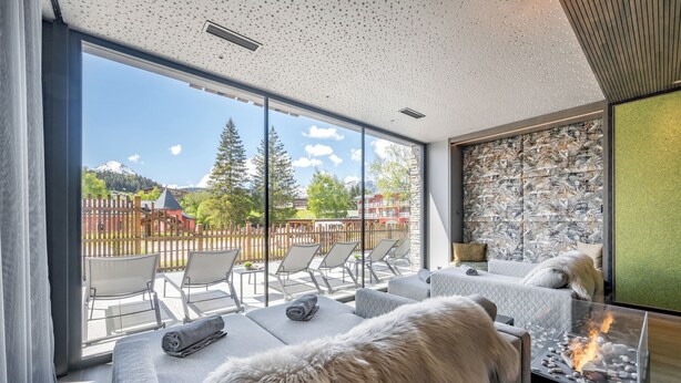 A modern room with a glass wall, a fireplace, and a view of a mountain.