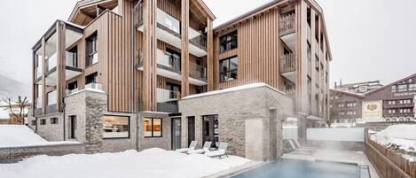 Un edificio moderno de varios pisos con zona de piscina, detalles de piedra y paneles de madera.