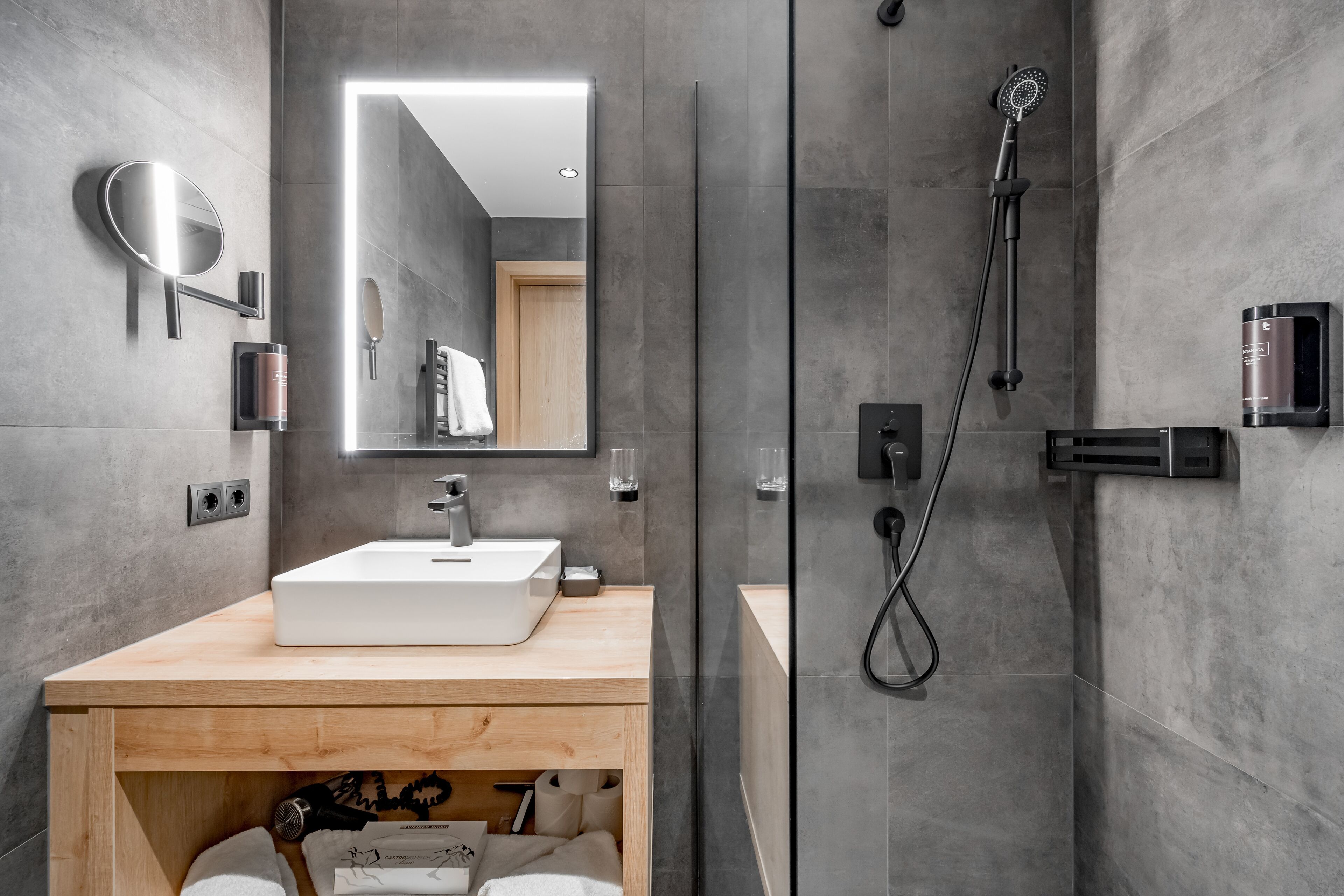 Ein modernes Badezimmer mit einem großen Spiegel, einem Waschbecken, einer Dusche und einem Schminktisch mit Handtuchhalter.