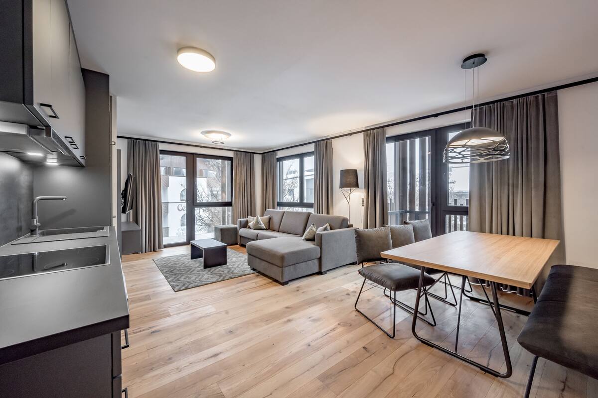 A modern living room with a sofa, a dining table, and a kitchen area.